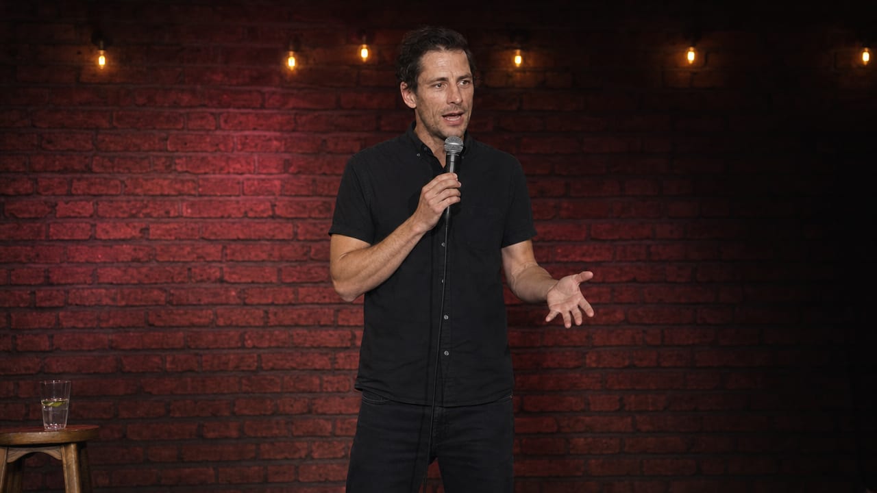 A comic mid-bit on a small dark stage, seen wide